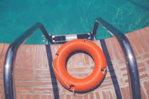 Orange lifebuoy or ring buoy on edge of swimming pool next to staircase