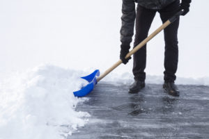 Man cleaning snow with blue shovel from ice surface for ice skating.